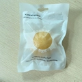 Gelber Konjac-Gesichtsschwamm in Bio-Verpackung auf einer hellen Holzoberfläche - Beutelverpackung / Ingwergelb