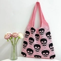 Pink knitted tote bag with black skull pattern hanging next to pink roses - Pink and Black