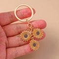 Golden metal keychain with three pastoral sunflower pendants held by hand on beige background - Sunflower