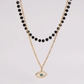 Detail van gelaagde gouden ketting en zwarte kralen met boze oog kristallen hanger - Ketting