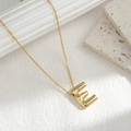 Minimalist gold balloon initial E pendant necklace for women on a white stone background - Letter E
