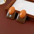 Primer plano de pendientes geométricos de resina en marrón y naranja sobre fondo cuero - Café (Pin de plata)