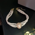 Gros plan du collier choker triple rang de perles avec pendentif ovale et chaîne dorée - 86# Collier - Collier de perles ovales dorées à trois couches