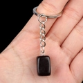 Hand holding a square black crystal stone keychain with a silver metal link and ring - Obsidian