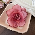 Gros plan d'une pince à cheveux fleur en organza rose poudré sur un plateau beige - Rouge