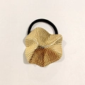 Dettaglio di un elastico per capelli con fiore dorato martellato e fascia elastica nera - Piastra Metallica con Texture Irregolare