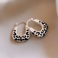 Macro detail of U-shaped silver hoop earrings with black leopard print on beige silk - Ear Buckle - Silver Geometric Leopard Print