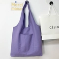 Minimalist purple canvas tote bag with front pocket and shoulder straps shown on white wall - Purple