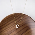 Collar de titanio dorado con colgante de letra C en nácar sobre bandeja de nogal - Letra C