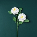 Nahaufnahme einer handgehäkelten weißen Rose mit gelbem Staubblatt und grünen Blättern - Weiße Gardenienzweig