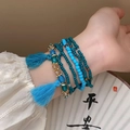Gros plan de bracelets en perles bleues avec pompons et détails dorés au poignet - Style de Gland Multicouche de Perles de Riz Bleues