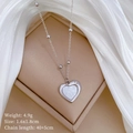 Close-up of heart pendant with shell inlay and small crystal on white satin fabric - Silver