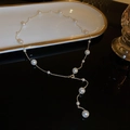 Elegante collana a Y dorata con perle bianche su un vassoio di ceramica di lusso - Collana - Oro