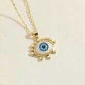 Detail of gold evil eye pendant necklace with blue eye core on textured fabric - Eyelash Design 1