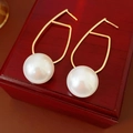 Dettaglio di orecchini geometrici dorati con perla bianca su una scatola di legno - Perno in Argento-Oro-Bianco