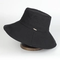 Black cotton bucket hat with large brim and gold metal plaque on a wooden stand - Adjustable / Black