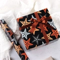Black gift wrapping paper with orange starfish patterns and a brown satin ribbon bow - Starfish; 80g Coated Paper