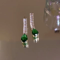 Vue macro de clous dorés avec zircon rectangulaire et gemme verte sur une surface réfléchissante - Boucles d'oreilles-Aiguille d'argent-Or (Cristal Vert)