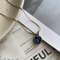 Primer plano de cadena de serpiente dorada con colgante de corazón azul sobre cerámica - Azul
