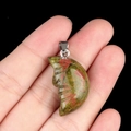 Unakite moon face pendant with silver clasp held by hand against black background - Unakite