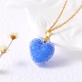 Détail macro du pendentif coeur en cristal bleu avec fine chaîne dorée sur fond blanc - Bleu foncé