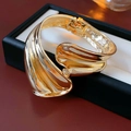 Makroaufnahme des hochglänzenden goldenen Spiralarmreifs mit unregelmäßigem Wellendesign - Gold