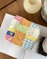 Quilted floral patchwork storage pouch displayed on an open book in a home setting - Colorful Grid / Patchwork