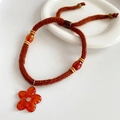 Detalle de collar artesanal con colgante de flor naranja y cordón trenzado marrón - Estilo de flores color café