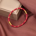 Close-up of red enamel and gold bamboo-style stainless steel bracelet on red silk fabric - Red