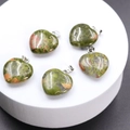 Green and orange natural stone heart pendants with metal clasps on a white stand - Unakite