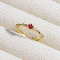 Macro shot of a gold ring with a red ruby center and side zirconias on beige fabric - Red Round Zircon with Accents (款式16)