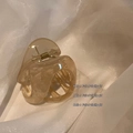 Pinza para el pelo de acrílico ámbar translúcido con muelle dorado sobre tela blanca - Beige