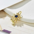 Macro di un ciondolo a girasole dorato con zirconi blu e bianchi su sfondo bianco - Blu scuro
