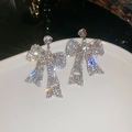 Makroaufnahme von silbernen Schleifenohrringen mit glitzernden Strasssteinen und Sterneneffekt - Silbernadel Schleife Ohrringe / Silber