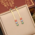 Golden long chain earrings featuring colorful evil eye beads on a beige leather jewelry box - Earrings