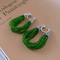 Close-up of green beaded hoop earrings with zircon-studded silver buckle on an open book - Green