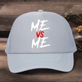Graue Mesh Trucker Cap mit ME VS ME Aufdruck und verstellbarem Riemen auf Holzgrund - Einheitsgröße / Grau