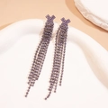 Détail de boucles d'oreilles géométriques à pompons et strass violets sur plateau blanc - Croix / Violet