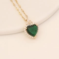 Macro detail of heart-shaped green crystal necklace with gold chain on a minimalist plate - Malachite green