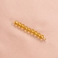 Makroaufnahme von bernsteinfarbenen Kristallperlen mit goldenen Ringen auf rosa Stoff - Champagner