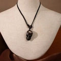 Detailed view of Maori style dark brown skull pendant on black braided cord necklace - Skull