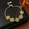 Dettaglio macro del bracciale vintage dorato a fiori con pietre di zircone verde - verde oliva