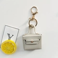 Detailed view of beige leather mini bag keychain with golden metal clasp on white background - Space Gray