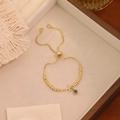 Dettaglio del bracciale regolabile con perline dorate, croce di cristallo e occhio greco - Stile Croce (T)