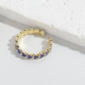 Detail eines verstellbaren Goldrings mit blauen Emaille-Herzen auf Texturfläche - Königsblau