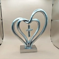 Detalle de escultura de corazón plateado con cruz colgante sobre una base rectangular fija - Plateado