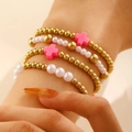 Dettaglio di un set di quattro bracciali a strati con perline dorate e croci rosa - Stile Croce Rosa (G-464)
