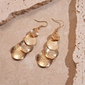 Macro shot of matte gold tiered circular drop earrings on a textured stone surface - Gold