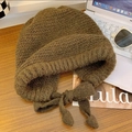 Deep olive green chunky knit earflap beanie with braided ties on a stylized desk - Solid Color-Coffee