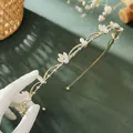 Close-up of golden leaf headband with delicate pearls and white floral petal details - Cat Eye Small Crown Flower